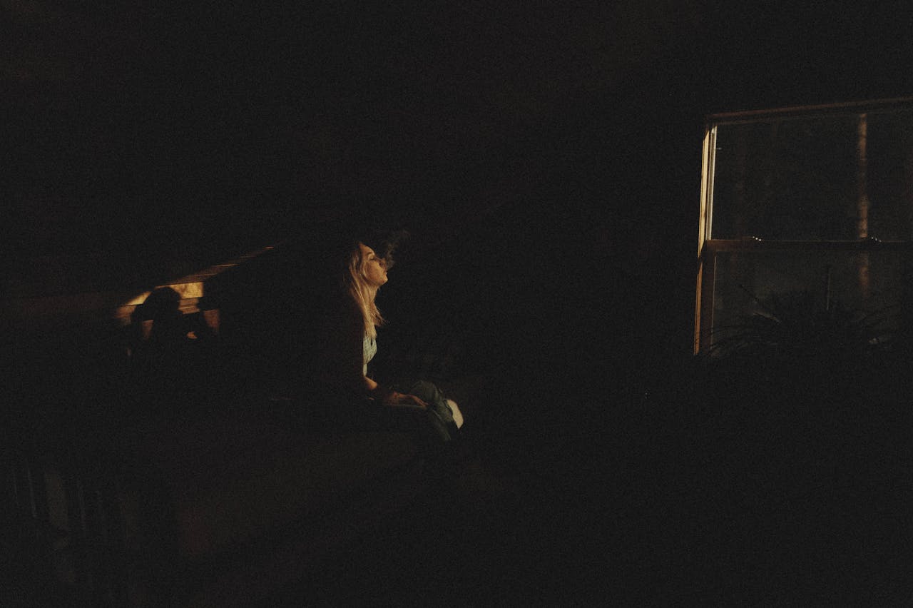 Silhouette of a woman sitting by a window at night, creating a mysterious ambiance.